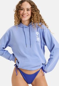 Svetlomodrá mikina s kapucňou a šnúrkou, predná vrecko a kvetinové vzory, v kombinácii s rebrovanými modrými bikiny. Mäkkučká tkanina, voľný strih.