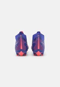 Botas de fútbol moradas con un diseño texturizado, detalles rosas en el talón y la suela, y una forma aerodinámica para un mejor rendimiento en el campo.