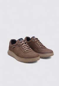 Baskets en daim marron avec semelle en caoutchouc crème texturée, bout rond et lacets plats. Présente une étiquette de logo et un design minimaliste.