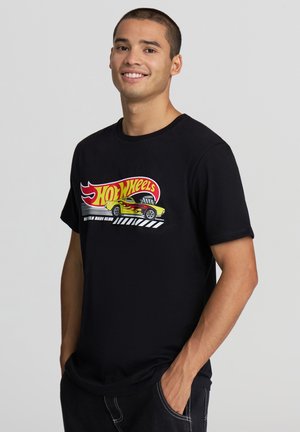 T-shirt nera in cotone con una grafica colorata "Hot Wheels" che presenta fiamme e un design di auto. Collo rotondo e maniche corte con una vestibilità comoda.