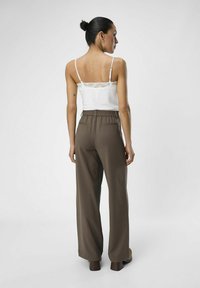 Brune vide bukser med elastisk talje, parret med en hvid camisole med blondekant. Glat stof med minimal dekoration.