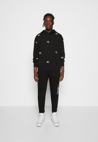 Felpa nera con piccoli accenti del logo bianco, abbinata a pantaloni jogger neri. Entrambi gli articoli hanno una vestibilità comoda e una texture morbida. Sneakers bianche completano il look.