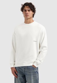 Witte crewneck sweatshirt van een gladde stof, met een klein zwart logo op de borst en geribde manchetten, gecombineerd met lichtblauwe jeans.