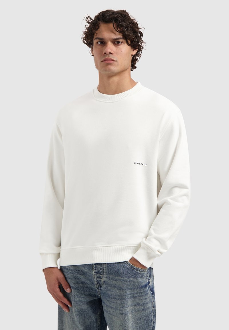 Witte crewneck sweatshirt van een gladde stof, met een klein zwart logo op de borst en geribde manchetten, gecombineerd met lichtblauwe jeans.