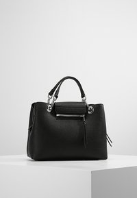 Bolso de mano de cuero negro con forma estructurada, herrajes plateados, un bolsillo con cremallera y borlas laterales. Textura lisa con acabado mate.