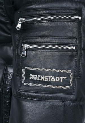 Pantalons en cuir noir avec plusieurs poches zippées argentées et une finition texturée. Comprend une étiquette cousue portant la mention "REICHSTADT™."