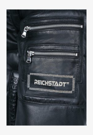 Pantalons en cuir noir avec plusieurs poches zippées argentées et une finition texturée. Comprend une étiquette cousue portant la mention "REICHSTADT™."