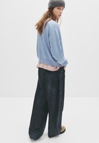 Felpa azzurra chiara, indossata sopra una maglietta rosa, abbinata a jeans scuri a vestibilità ampia. Un berretto lavorato a maglia grigio e calzature piatte completano il look.