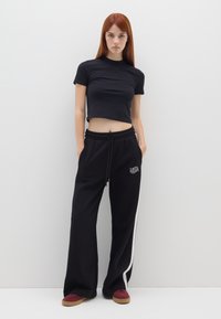 Camiseta negra corta combinada con joggers negros sueltos que presentan franjas laterales blancas y detalle bordado "USA". Calzado casual completa el look.