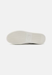 Suola di sneakers in gomma bianca con un pattern di grip testurizzato e logo impresso, caratterizzata da un design liscio e una forma arrotondata.