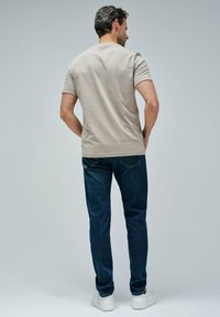 Beige bavlněné tričko a tmavě modré džíny. Tričko má kulatý výstřih a krátké rukávy. Džíny mají rovný střih a standardní velikost.
