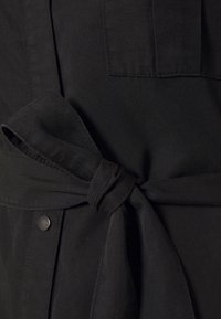 Svart tygplagg med knytskärpa. Slät struktur med en elegant design och en silverfärgad tryckknapp.