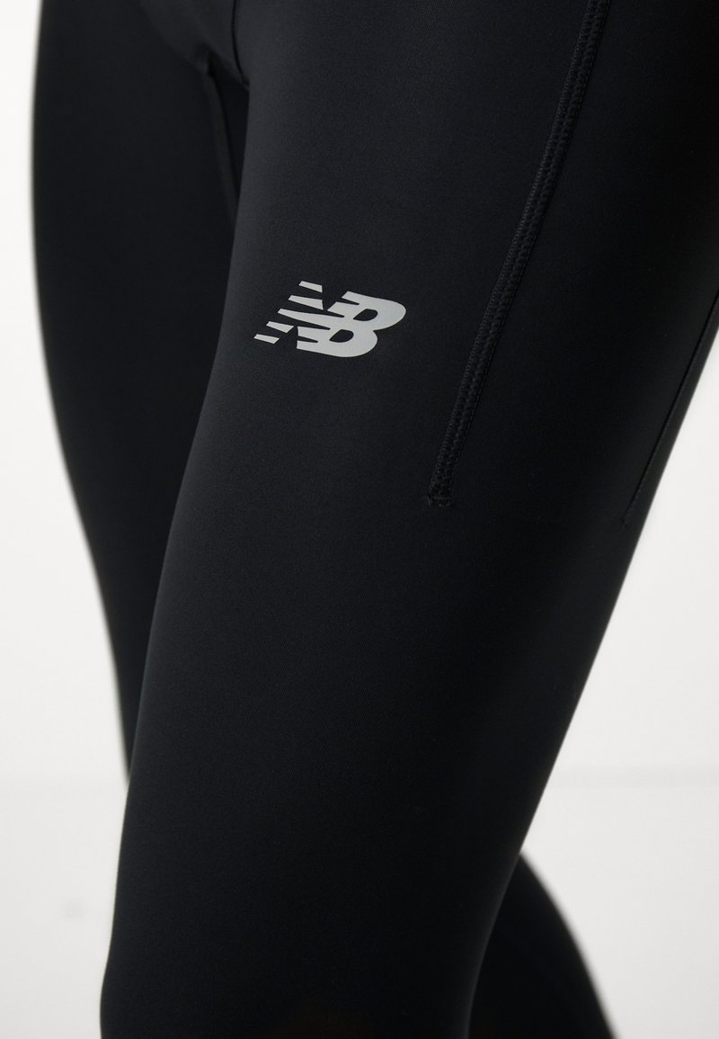 Leggings de sport noirs avec une texture lisse, présentant un logo argenté New Balance sur le côté et un design ajusté pour le confort.
