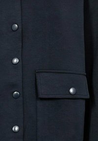 Marineblauw shirt met een gladde textuur, voorzien van metalen grijze knopen en een klepzak. Het ontwerp heeft een voorzijde met knopen en nette stiksels.