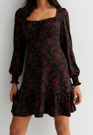 Robe noire à motif floral, avec manches longues, encolure carrée et ourlet à volants. Elle présente un motif de fleurs rouges et vertes. Texture du tissu lisse.