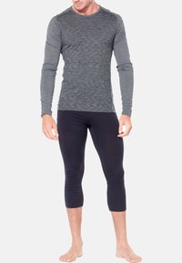 Långärmad atletisk topp i mörkgrått med texturerade vågor, parat med åtsittande svarta capribyxor. Båda är tillverkade av elastisk tyg.