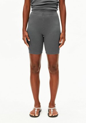 Persoon die grijze geribbelde knielange shorts en bijpassend top draagt, staat met ontspannen armen langs het lichaam en draagt witte touwsandalen.