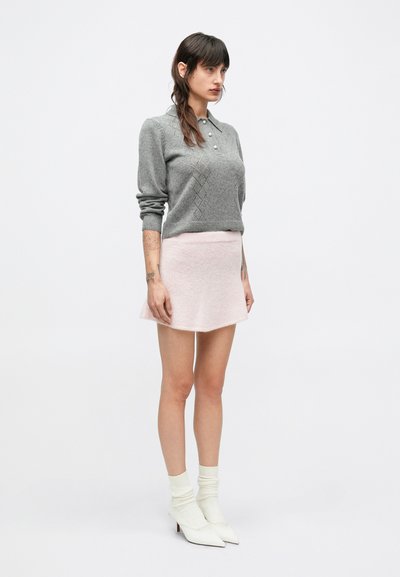 Sivý pletený sveter s polokolárom a diamantovým vzorom, doplnený svetloružovou rozšírenou sukňou. Modelka má na sebe biele špicaté lodičky a ponožky.