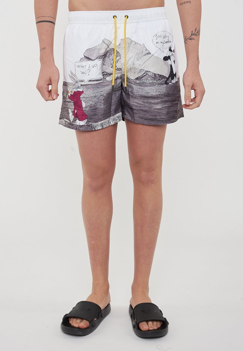 Pantaloni da bagno bianchi con un design grafico che presenta personaggi dei cartoni animati. Vita elasticizzata con cordino giallo. Il motivo include montagne e acqua.