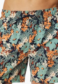 Mannen zwembaden met een bloemenpatroon in groen, oranje en marineblauw, voorzien van een elastische tailleband en een verstelbaar trekkoord.