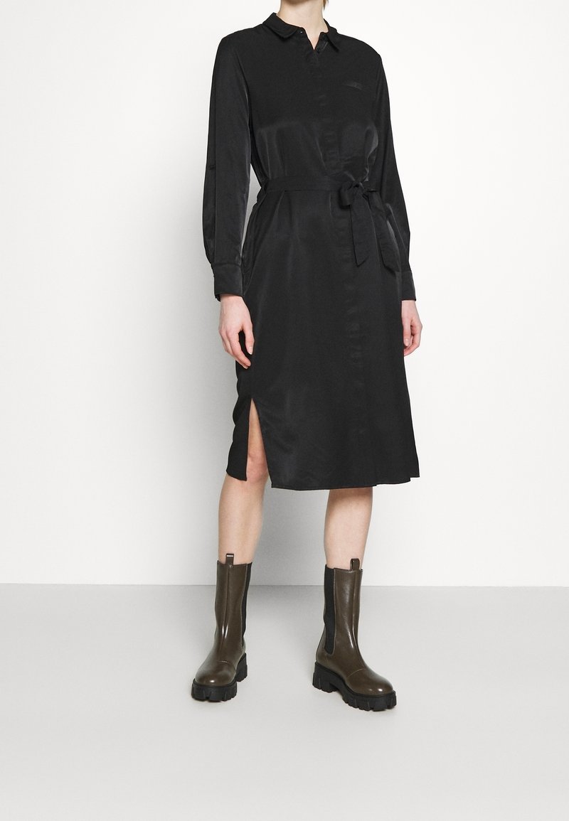 Svart, långärmad knapp-up klänning med knyt i midjan, sidoflitsar och mjuk textur. Kombinerad med bruna ankle boots med texturerade paneler.