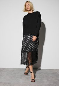 Black sweatshirt over a polka dot skirt with lace hem. The skirt features white dots, while the lace adds texture. Worn with black sandals.