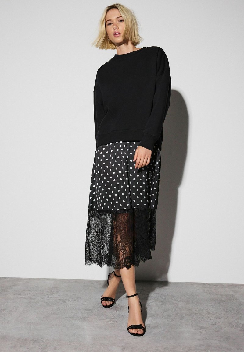 Black sweatshirt over a polka dot skirt with lace hem. The skirt features white dots, while the lace adds texture. Worn with black sandals.