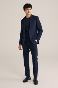 Mornarsko suknjo s krojenim sakom in ožjimi hlačami, nosi prek ujemajoče se majice s kratkimi rokavi. Sijajni črni loafers in srečna ura dopolnjujeta videz.