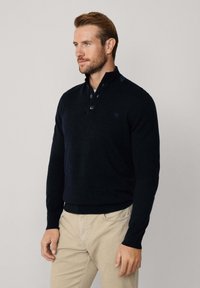 Granatowy sweter z półzamkiem i zapięciem na trzy guziki. Posiada ściągacze przy mankietach i dolnej k.Rawie, a na piersi znajduje się małe wyszywane logo.