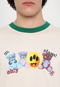Three colorful teddy bears with button eyes and a yellow smiley face with fangs on a beige shirt with green collar.