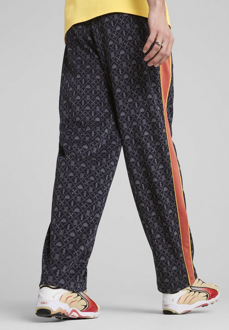 Pantalons noirs à motif géométrique, avec une bande latérale orange contrastante. Portés avec des baskets colorées.