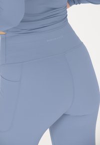 Ljusblå högmidjade leggings tillverkade av stretchigt material, med en sidficka och diskret logotyp på midjebandet.