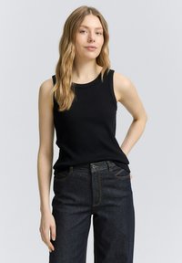 Top negro sin mangas con escote redondo, combinado con jeans de mezclilla oscuros de cintura alta. Tejido liso y ajustado con detalles mínimos.