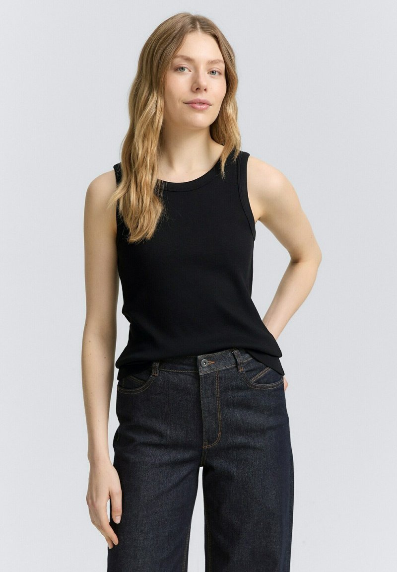 Top negro sin mangas con escote redondo, combinado con jeans de mezclilla oscuros de cintura alta. Tejido liso y ajustado con detalles mínimos.