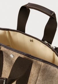 Brązowa torba na ramię z ciemnobrązowymi uchwytami, skórzanym wykończeniem i beżową podszewką z metalowym zapięciem.