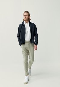 Svart zip-up jacka, vit polo skjorta, ljusgrön tajt byxor och vita sneakers. Släta texturer med minimalistisk design och subtila detaljer.