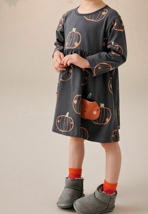 Robe grise à manches longues avec imprimé citrouille orange, dotée d'une taille froncée et agrémentée de détails verts et marron. Associée à des bottes grises.