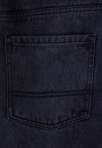 Black denim fabric featuring a single back pocket with double stitching and a clean, finished edge. Textured surface with subtle grain.