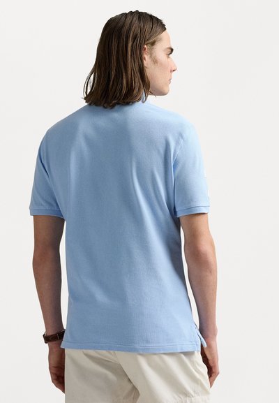 Light blue polo shirt made of soft cotton, featuring short sleeves, a straight hem, and side slits. Smooth texture with no visible patterns.