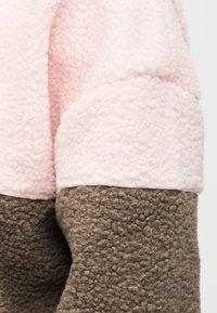 Τοπ από ύφασμα φλίς σε ανοιχτό ροζ με υφή, συνδυασμένο με σκουρότερο καφέ φλίς στο κάτω μέρος. Διαθέτει σχέδιο με χρωματικές μπλοκ.