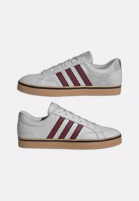 Zapatillas deportivas blancas de corte bajo con suelas de goma marrón y tres franjas rojo oscuro en cada lado, mostradas desde vistas interiores y exteriores.