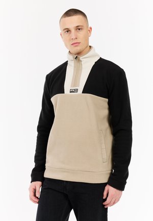 Pulóver de forro polar en negro y beige, con un cuello de media cremallera, tejido texturizado y un parche central con el logo. Incluye bolsillos laterales.
