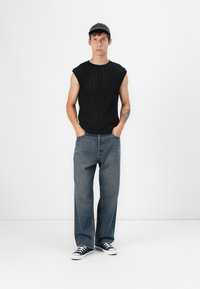 Sort ribbet strikket top uden ærmer, løstsiddende blå denim jeans og sorte kanvas sneakers med hvide såler. Enkel kasket båret bagfra.