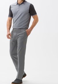 Polo à manches courtes en gris avec des manches noires, doté d'un col et d'accents rayés. Associé à un pantalon gris clair et des chaussures noires.