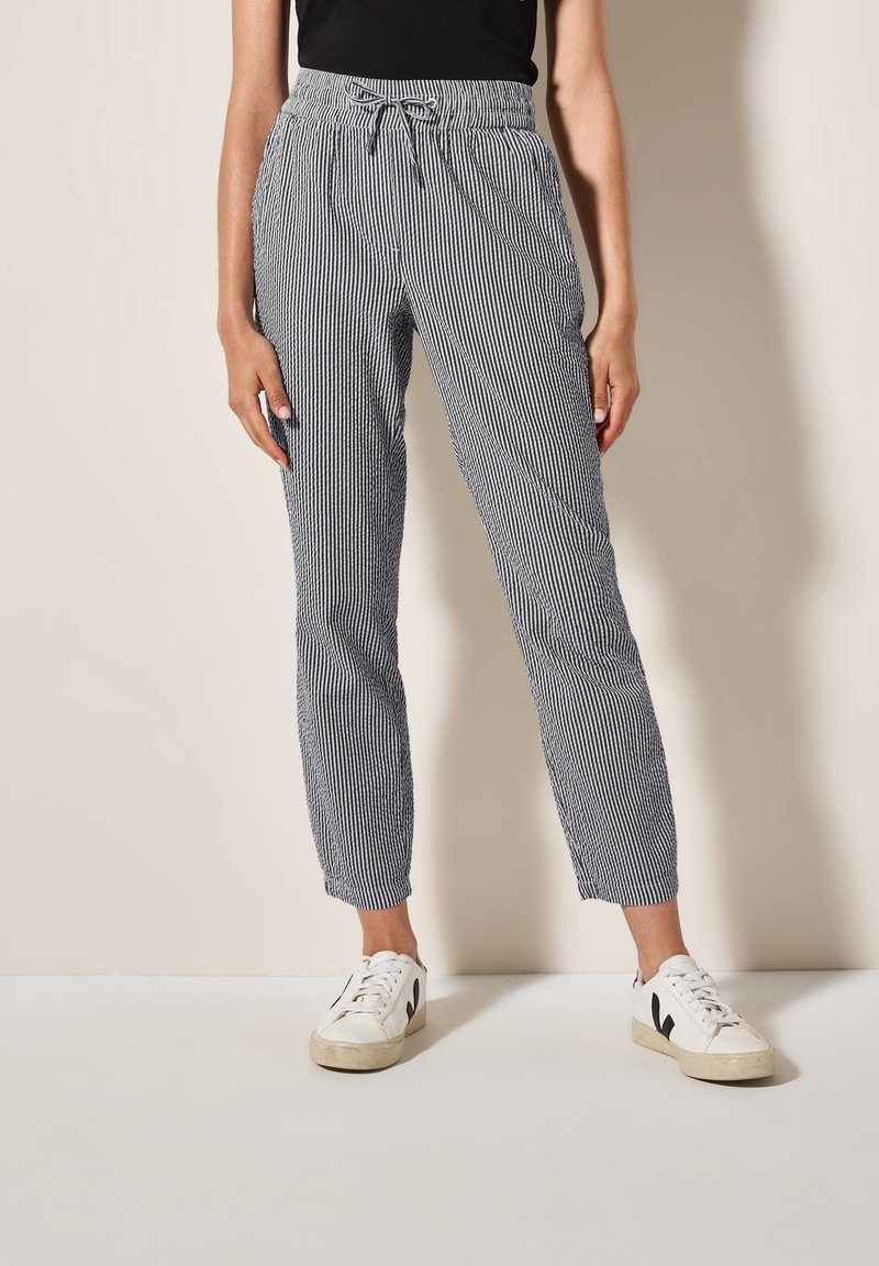 Pantalons rayés bleu marine et blanc, dotés d'une taille élastique avec cordon de serrage, des jambes effilées et un tissu léger et texturé.