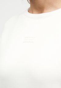 Ανοιχτό μπεζ φούτερ με στρογγυλή λαιμόκοψη, που διαθέτει μια μικρή, υφασμάτινη ετικέτα του brand ραμμένη στο στήθος. Λεπτό ύφασμα με ελάχιστες λεπτομέρειες.