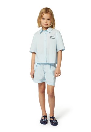 Lichtblauw shirt met korte mouwen en geborduurde tekst "Parijs", gecombineerd met bijpassende korte broeken en marineblauwe sandalen met decoratieve accenten.