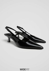 Crne lakirane slingback pete s oštrim nosovima i niskim kitten potpeticama, prikazane na bijeloj pozadini označene "Širi kroj."
