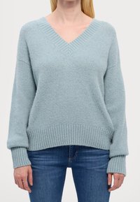Hellblau gestrickter Pullover mit V-Ausschnitt, gerippten Bündchen und Saum. Weiche Textur, lässige Passform, lange Ärmel. Kombiniert mit Jeans.