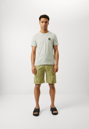 Light gray cotton T-shirt with short sleeves and a small black logo patch, paired with cargo shorts in olive green with pockets and buttons. Black sandals.